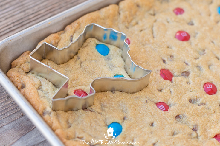 using a cookie cutter to cut the Texas shape out of the chocolate chip cookie dough