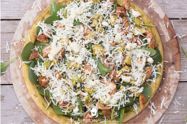 apple, chicken, and pesto pizza with all ingredients on top before placed in the oven